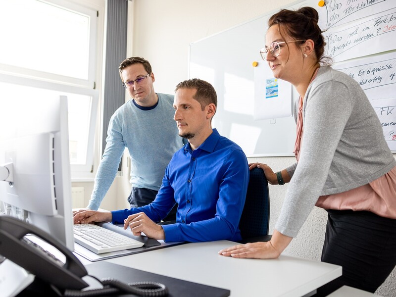 Drei Personen arbeiten gemeinsam an einem Computer in einem Büro.