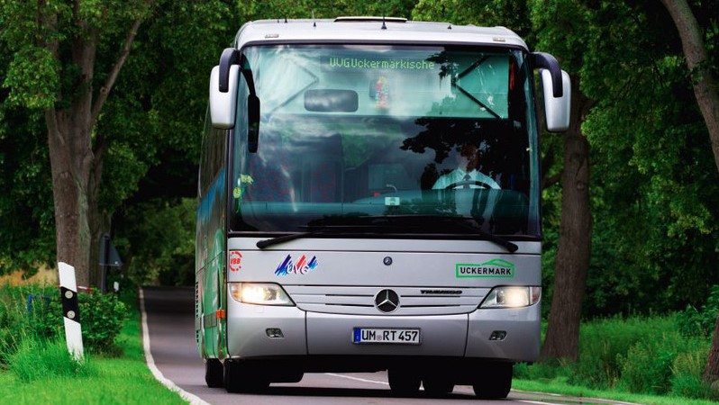 silberner Bus frontal in grüner Landschaft