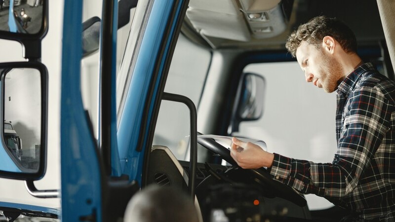 Mann schaut in Unterlagen in der Fahrerkabine eines Lkw