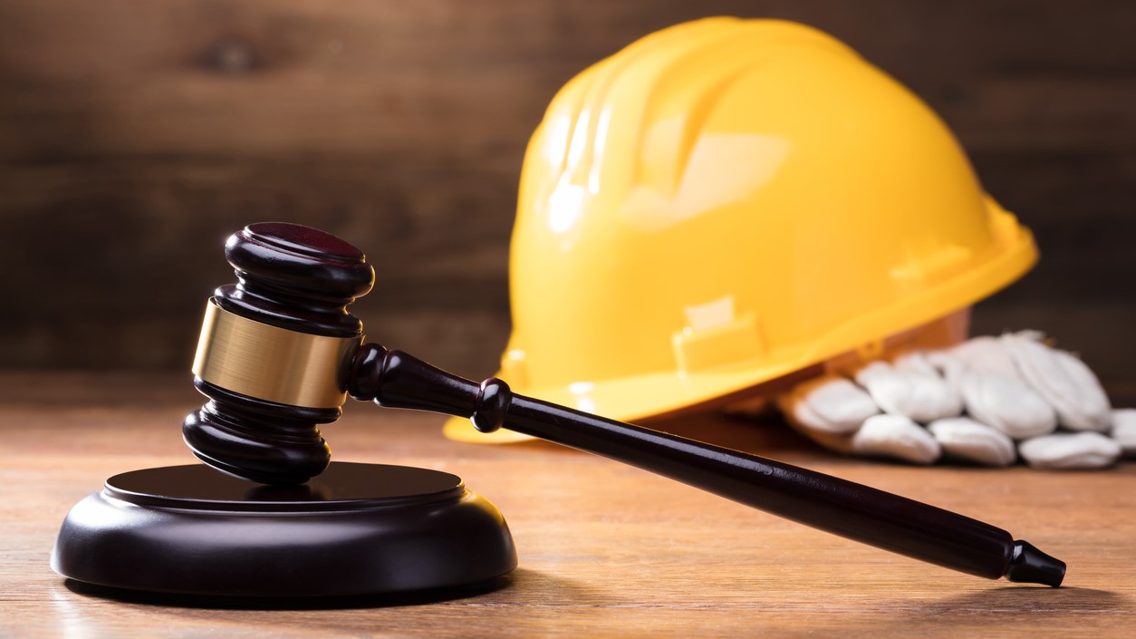 Sie sehen einen Richterhammer und gelber Bauhelm auf einem Holztisch