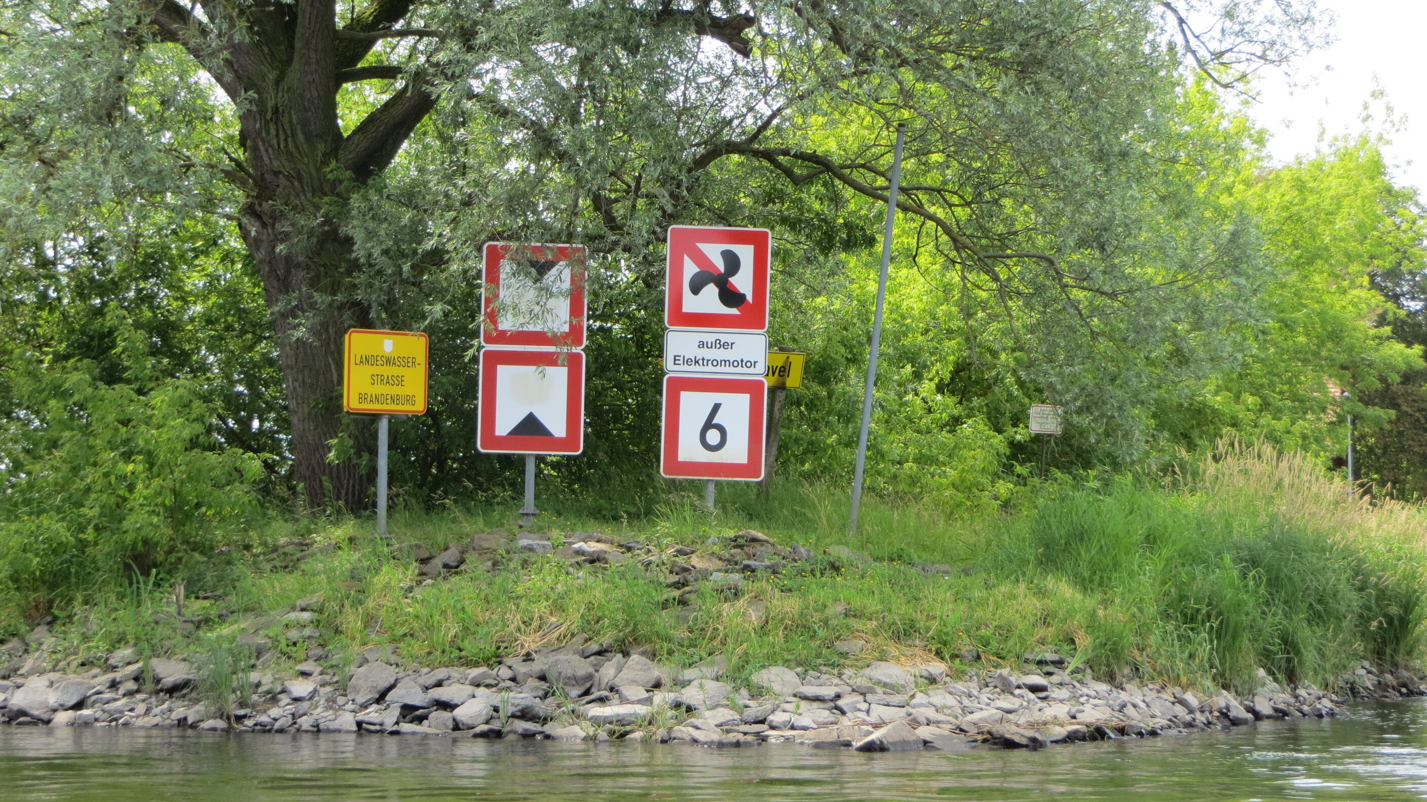 Bild: Ufer mit mehreren Schifffahrtszeichen an einer Wasserstraße in Brandenburg, darunter Hinweise zu Fahrverboten und Geschwindigkeitsbegrenzung für Boote.