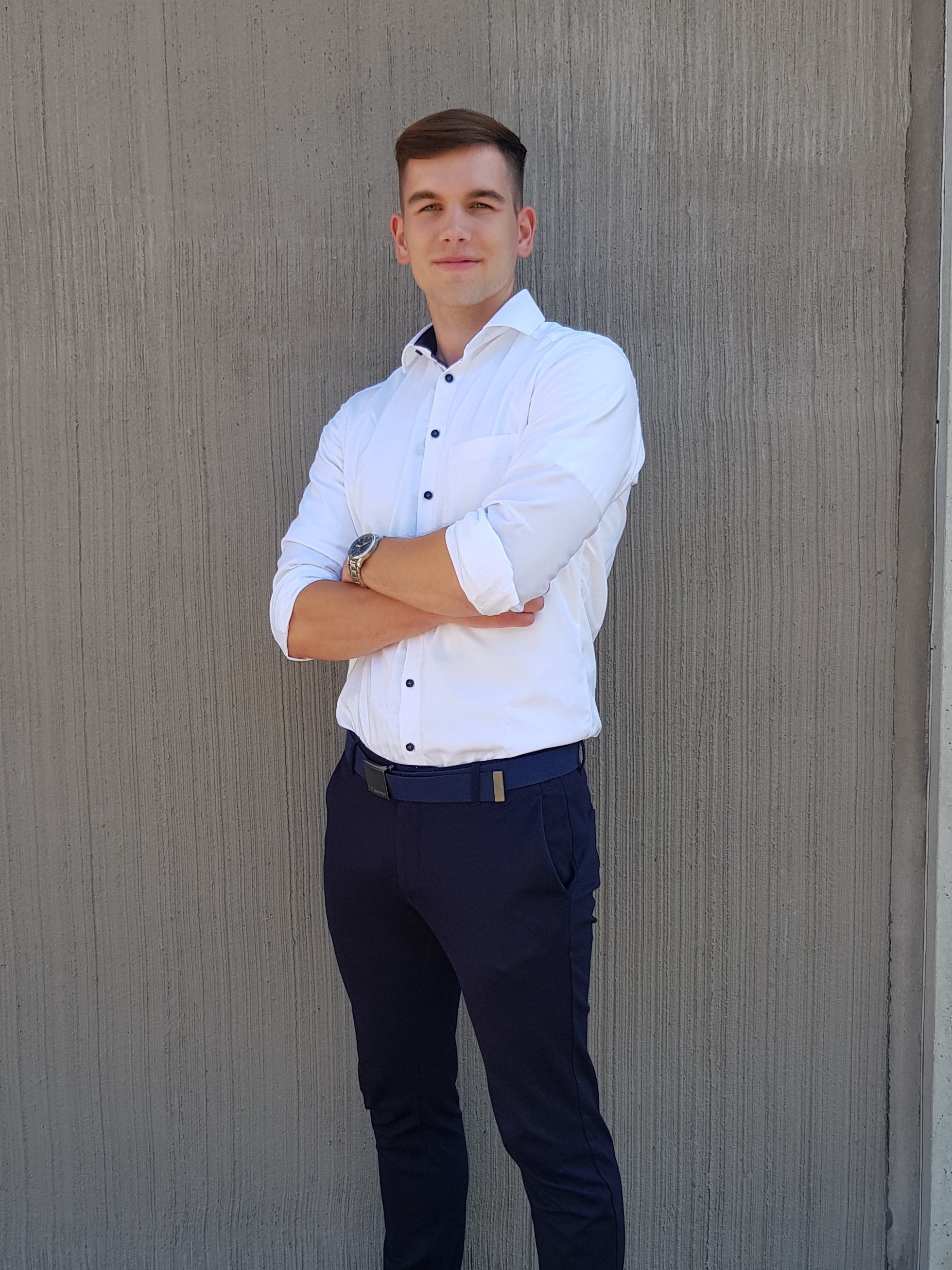 junger Mann steht mit eingeschränkten Armen vor einem Gebäude