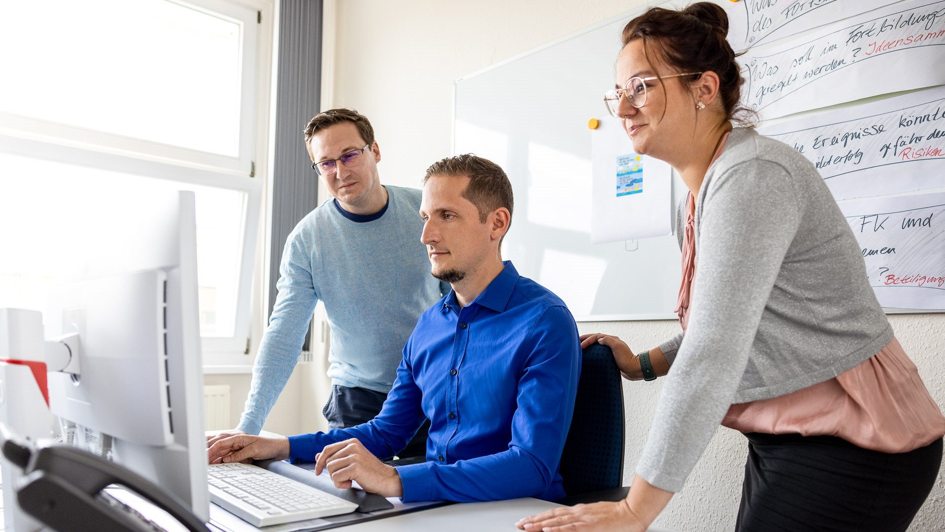 2 Männer und eine Frau schauen gemeinsam auf einen Computerbildschirm in einem Büro