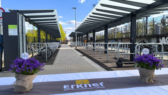 überdachte Fahrradabstellanlage am Bahnhof Erkner am Tag der Eröffnung, Vordergrund: Podium mit lila Blumen in Blumentöpfen, Hintergrund Zugang zum Bahnsteig